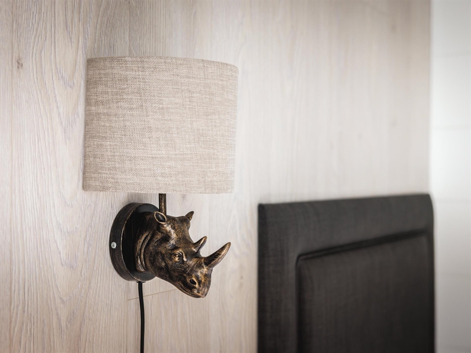 Wall-mounted bedside lamp with a bronze rhino head and grey lampshade.