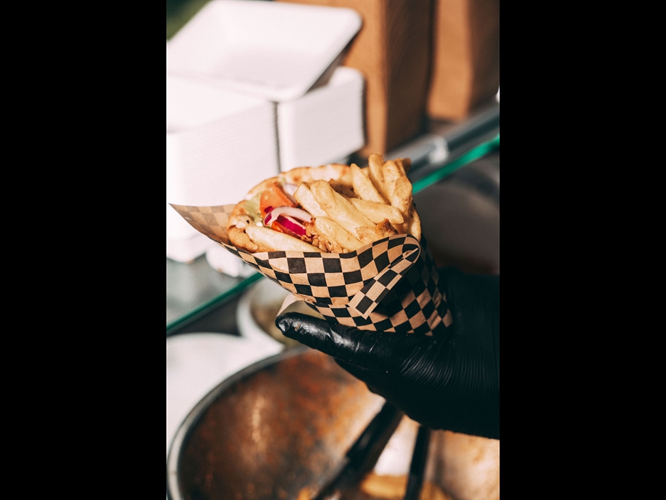 Street food wrap with fries and grilled meat being served at a food festival, fresh takeaway food in a checkered tray.