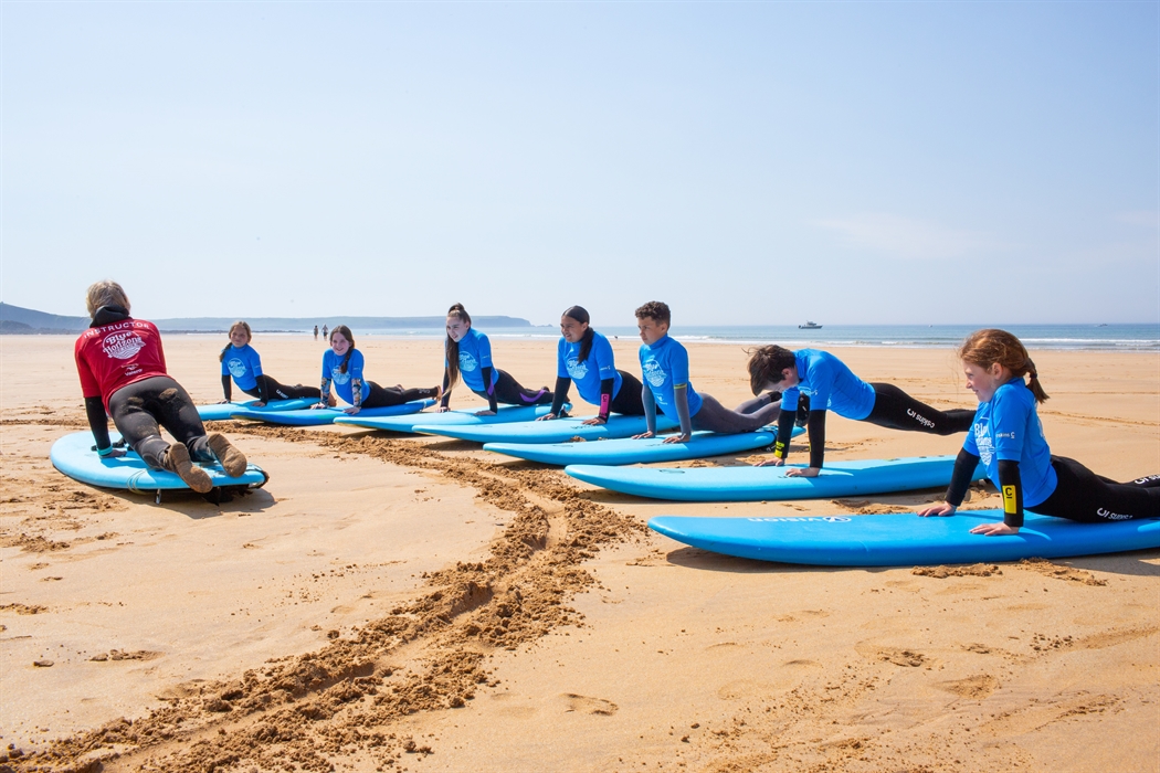 Group of children practising surf skills on the beach with a Blue Horizons instructor during a surf lesson in Pembrokeshire.