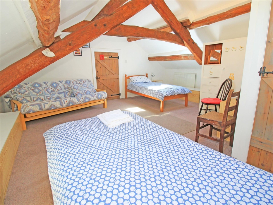 A large bedroom with exposed wooden beams having twin beds and extra double futon bed.