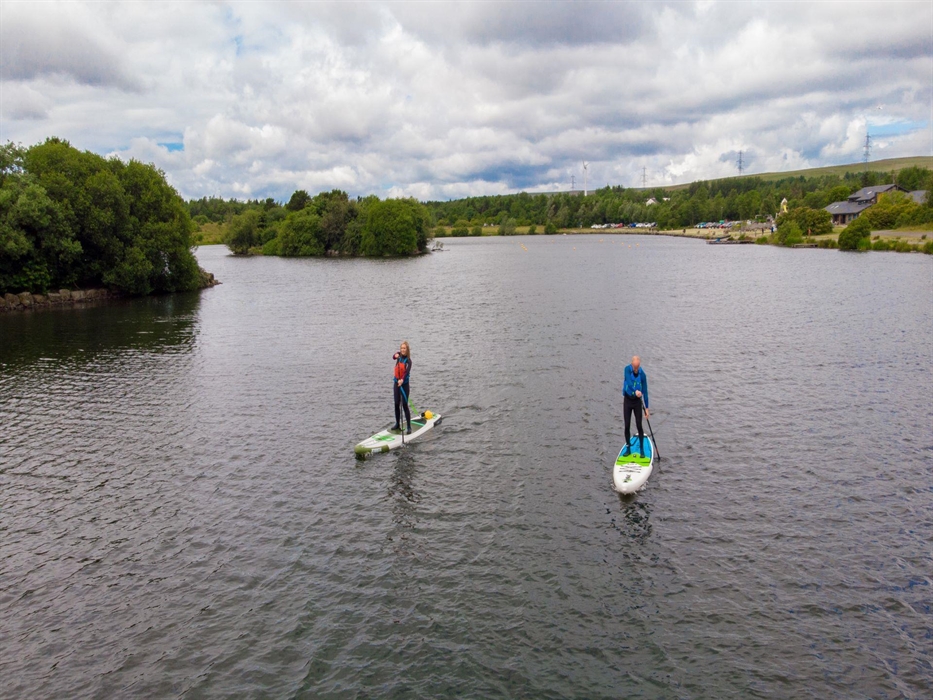 Visitors enjoying standup paddleboarding on the lake at Parc Bryn Bach.