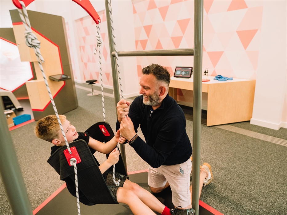 A father helps his son with an exhibit where you have to pull yourself up using ropes and pulleys.