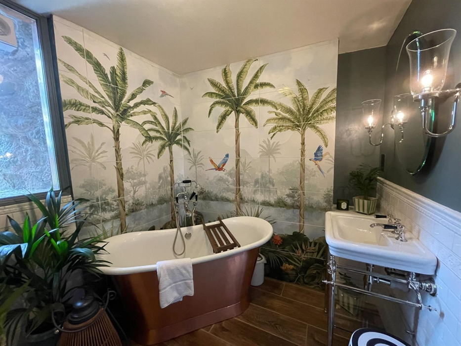 The family bathroom in the west wing of Ysgubor Degwm seadog and stone. A copper bath with white enamel inside, mural wall and wooden floor.