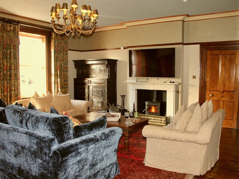 Lounge with three sofas, 2 large sash windows, woodturner and large tv.  2 chairs with a chess table