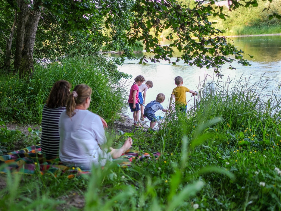 Parents sat on the riverbank watching children paddle and play in the river.