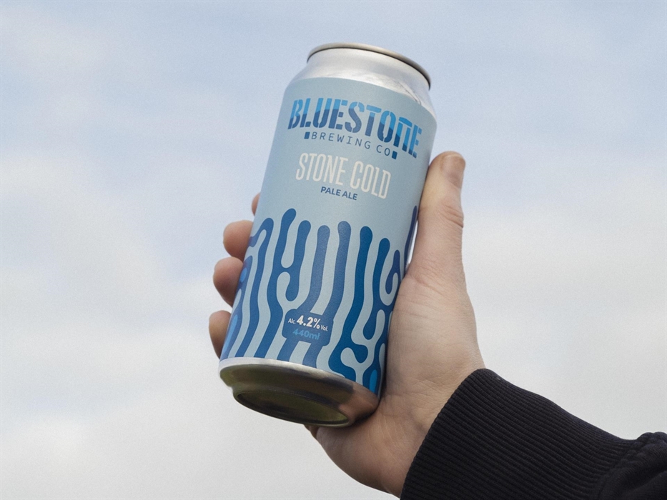 A hand holding up a can of beer to the sky, the label is blue with a swirly pattern on and read Stone Cold Pale Ale
