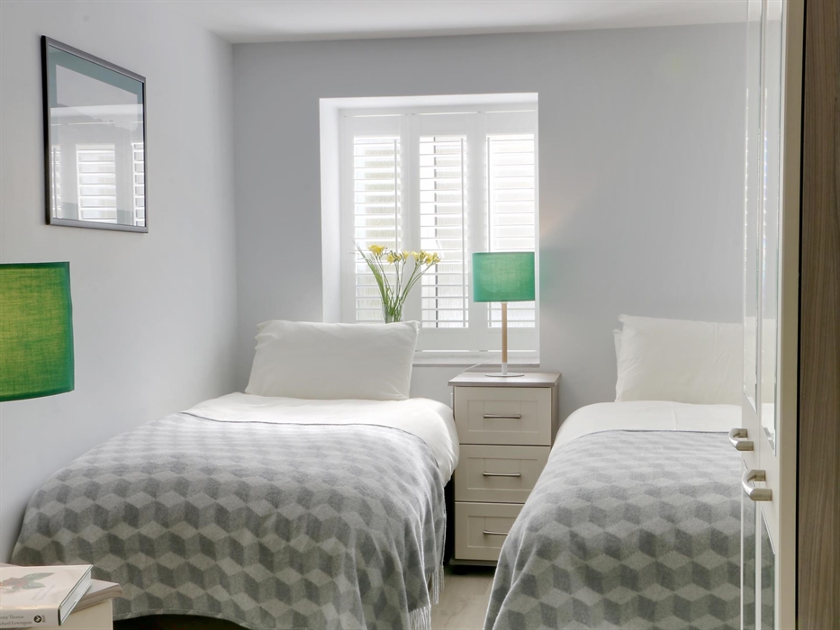 Twin bedroom with soft grey decor, mirrored wardrobe, and geometric bedding, filled with natural light from shuttered windows.