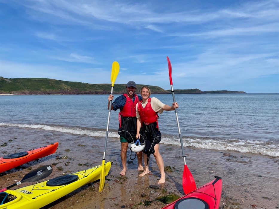 A happy couple standing by their sea kayaks at the end of a day on the sea