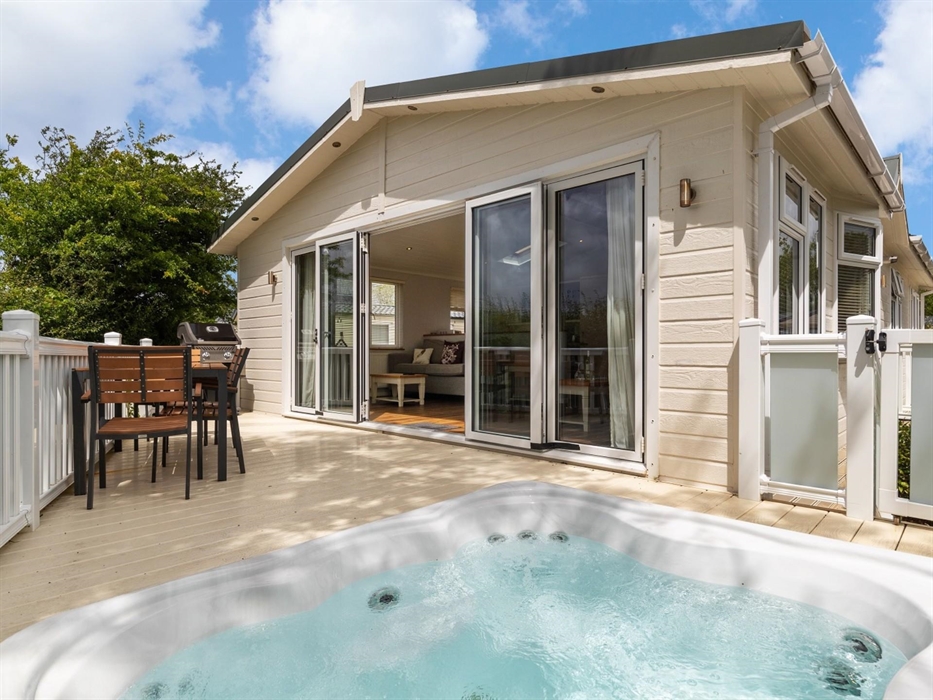 With view of large exterior doors, living area, private deck, hot tub, outdoor furniture and BBQ.