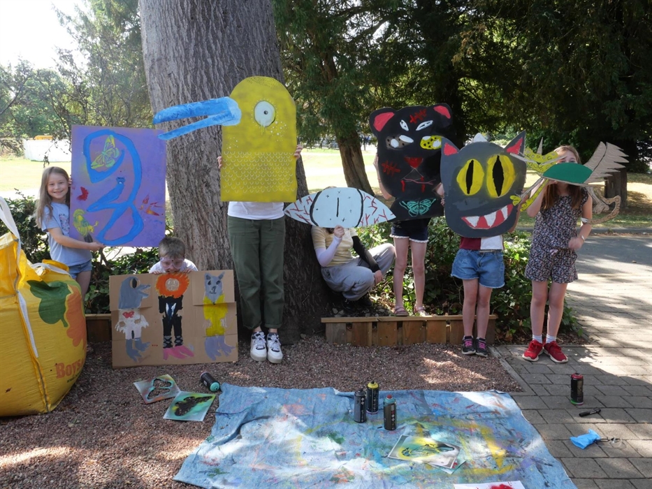 Children posed as part of their artworks, large scale brightly coloured drawings on cardboard. Creating a collaged scene of animals with their painted