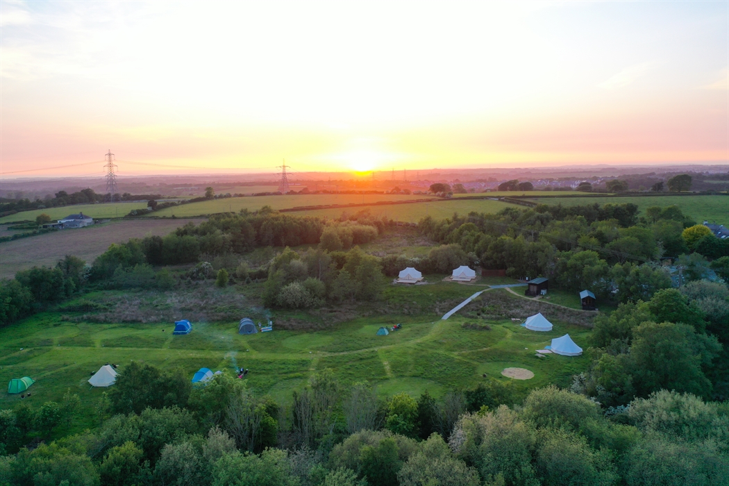 Birdseye view of the meadow camping area with tents and sunset in the distance over Anglesey