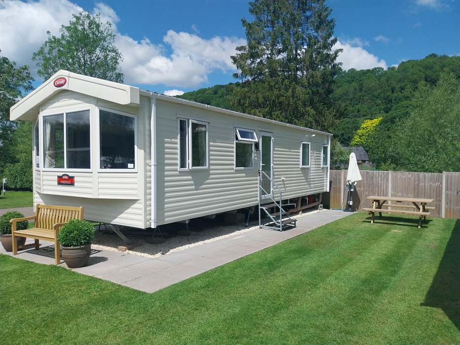 Static caravan with picnic bench outside with patio stones and freshly mowed grass parking area
