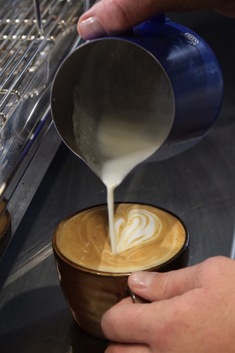 A close up of a barista's hands as they pour the last of the milk into a latte cup.