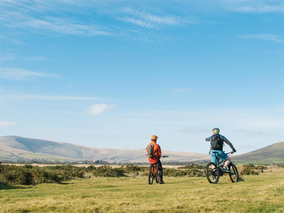Two mountain bikers look across the Preseli Hills on a sunny day with blue skies.