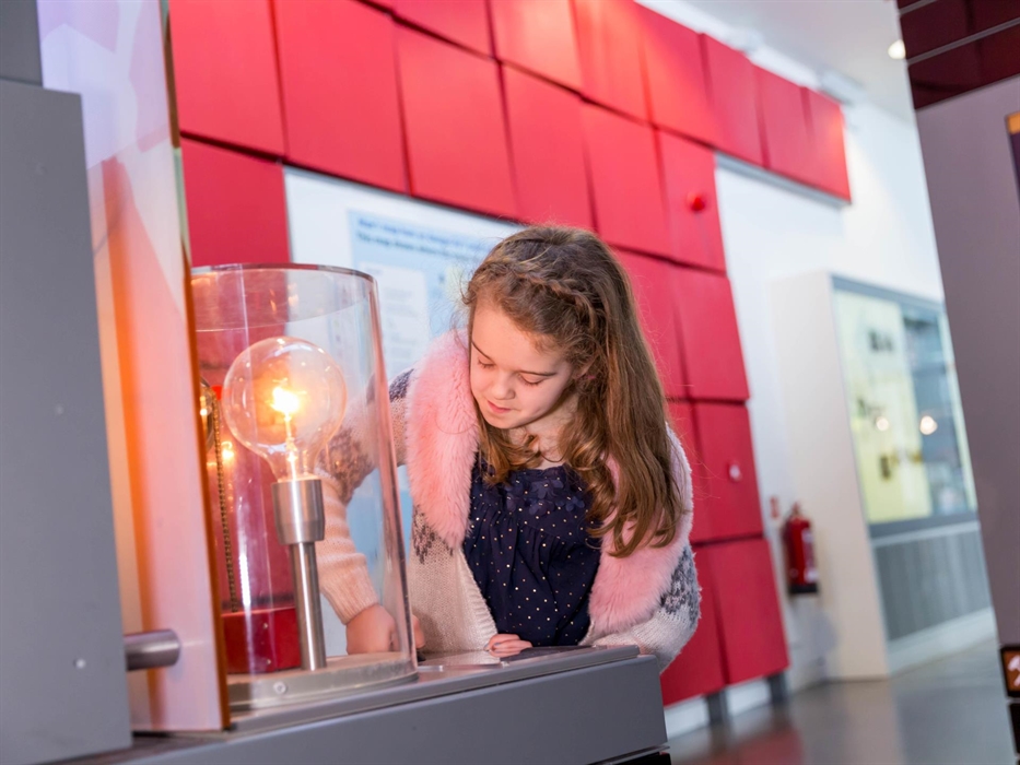 a young girl presses buttons in front of a large light bulb to make it glow.