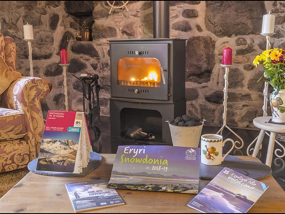 An ingle-nook fire place with candles and a Wood burn stove with a fire lit and a coffe table with some tourist information guides on things to do in