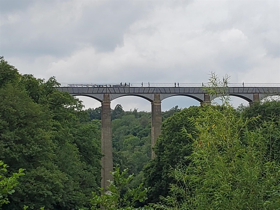 Looking at Pontcysylite Aqueduct from below, seeing the arches as people and a long boat cross