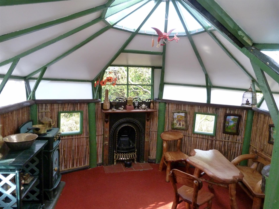 The interior of a play house in the garden, featuring home made child size furniture, a fire place and cooker