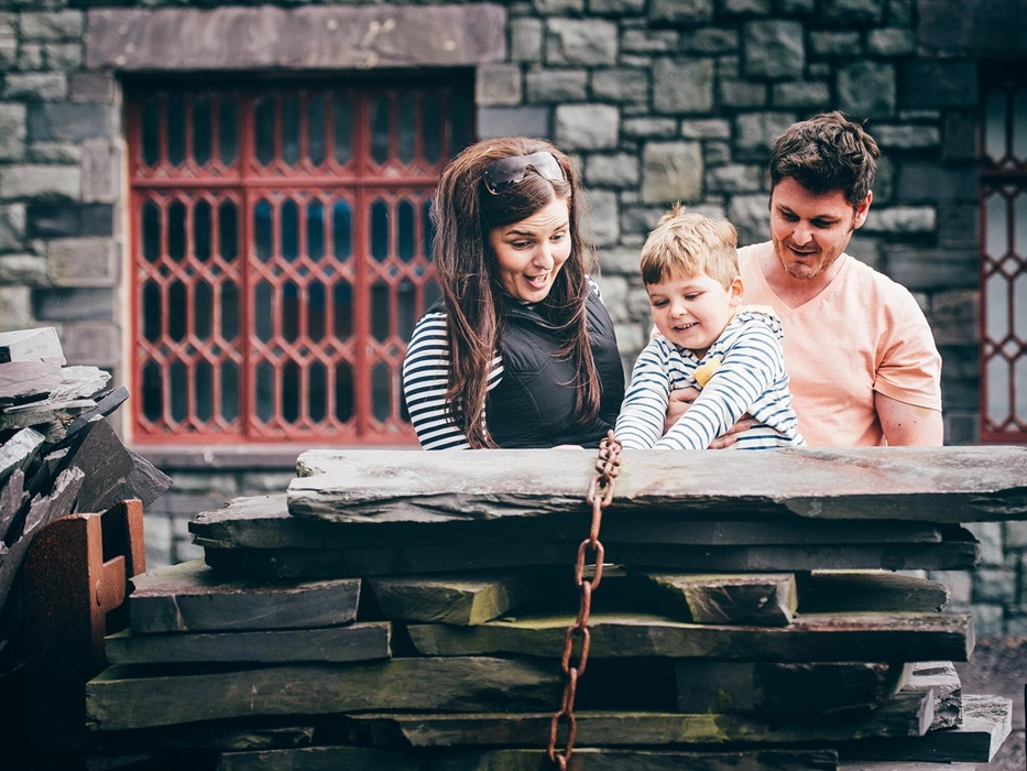 Parents and young son look at a pile of dressed slates piled onto a wagon in the workshop yard.