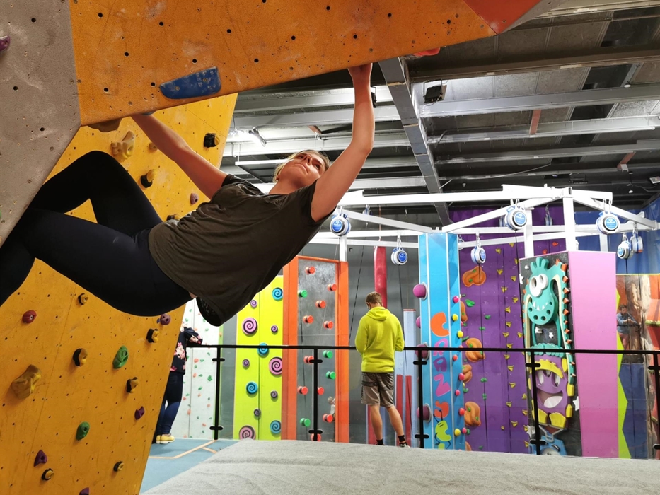 Woman climbs unroped over crash mats, while man watches CrazyClimb