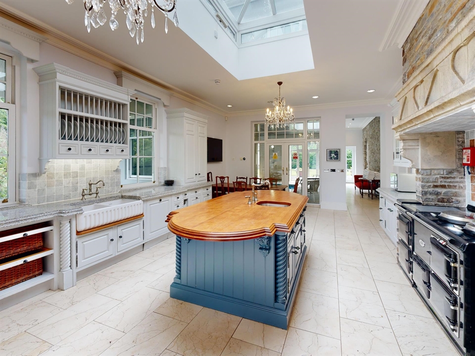 Traditional kitchen with stone fireplace, AGA range cooker, a large wooden island, and classic cabinetry, filled with natural light from a skylight an
