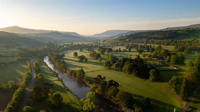 beautiful image of the Glanusk Estate landscape at sunrise with rolling fields with lots of trees, The River Usk running through and mountains in the
