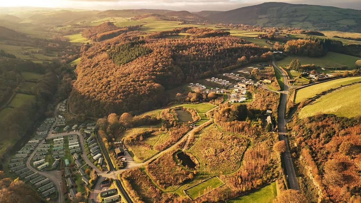 A photo of a woman relaxing on holiday, sat out on a sun lounger reading a magazine overlooking the Clywedog Valley.