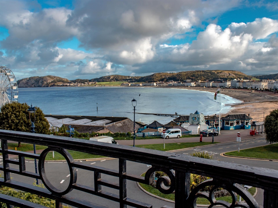 A beautiful coastal view from a balcony, featuring a sandy beach, a Ferris wheel, and a row of elegant seaside buildings.