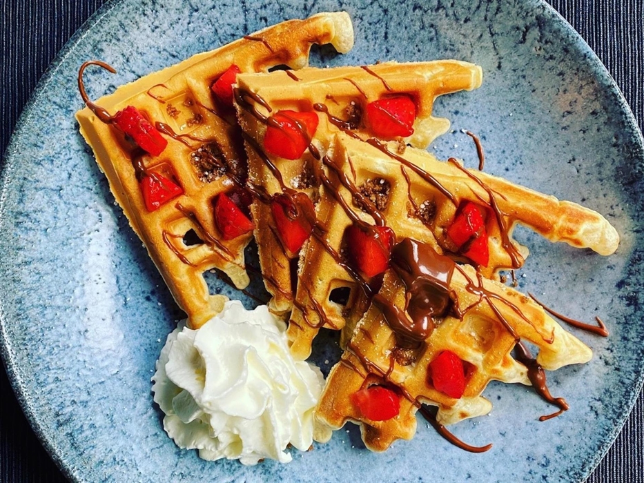 Waffles, strawberries, cream and chocolate sauce in a blue bowl