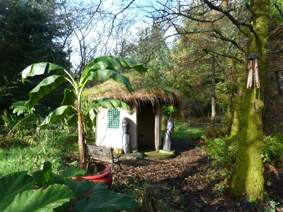 Jungle hut with turf roof and large African style carvings. Banana tree in the foreground