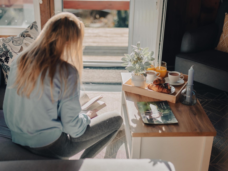 Immersed in a good read within the cosy confines of the lodge, surrounded by soft, inviting interiors that echo the peaceful ambiance of the Timber Hi