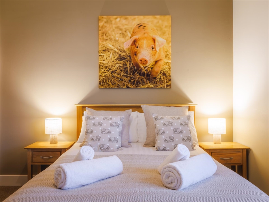 Large pig wall canvas above double bed and side tables with lamps and pig themed cushions and white fluffy towels.