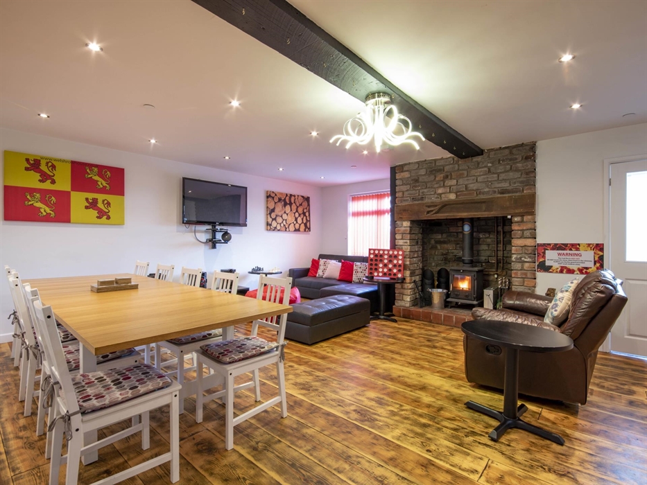 Welsh Row House with large living room and dining area with log ingle nook fireplace.  Wooden floor and seating area.  Large dining table that seats u