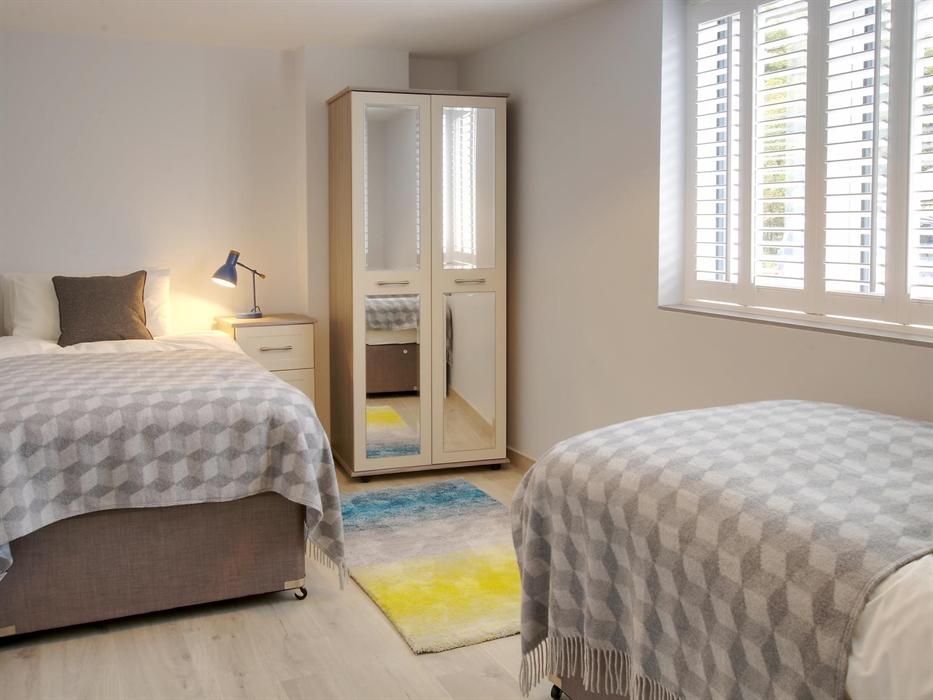 Twin bedroom with geometric throws, fresh white walls, and pops of colour from green lamps and fresh daffodils.