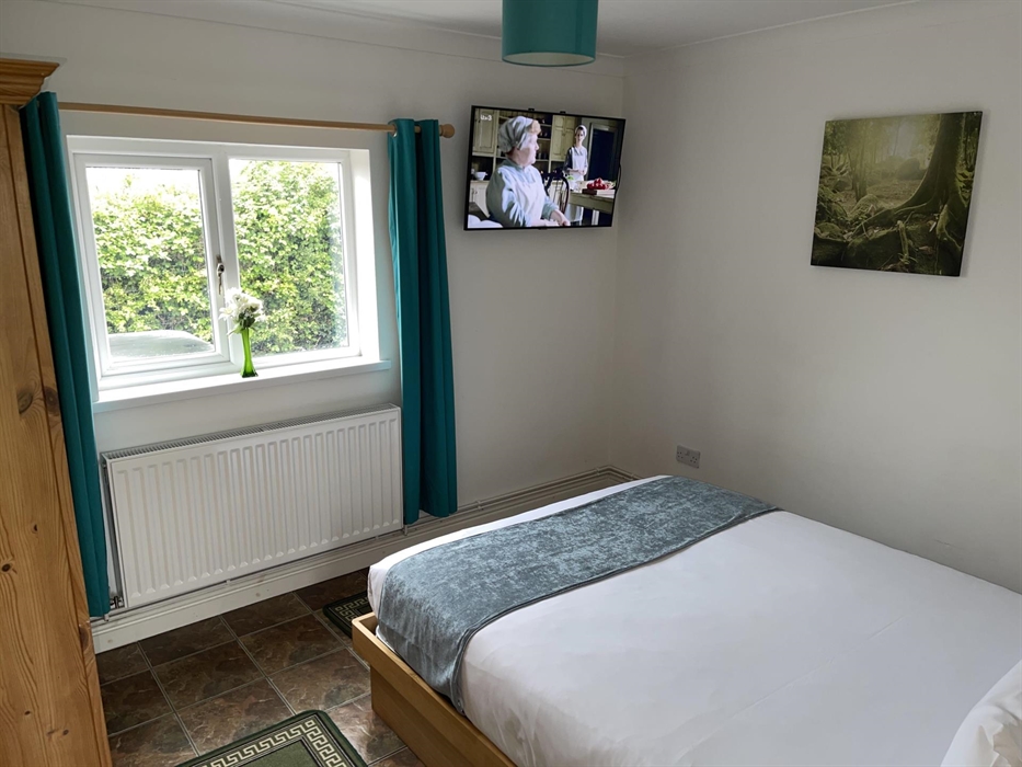 Main bedroom showing king size bed, pine wardrobe, window overlooking the private garden and a 43 inch Smart TV with Freeview channels, Catch up TV an