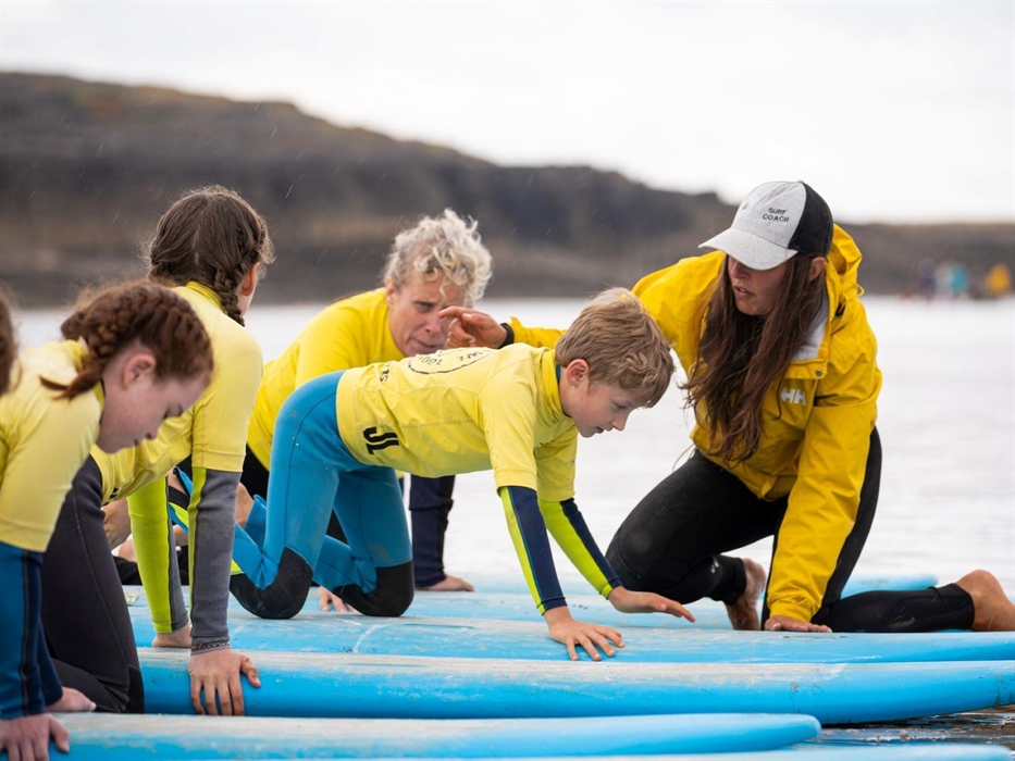 Image of students receiving a surf lesson on surf boards at the shores of the sea from an instructor.