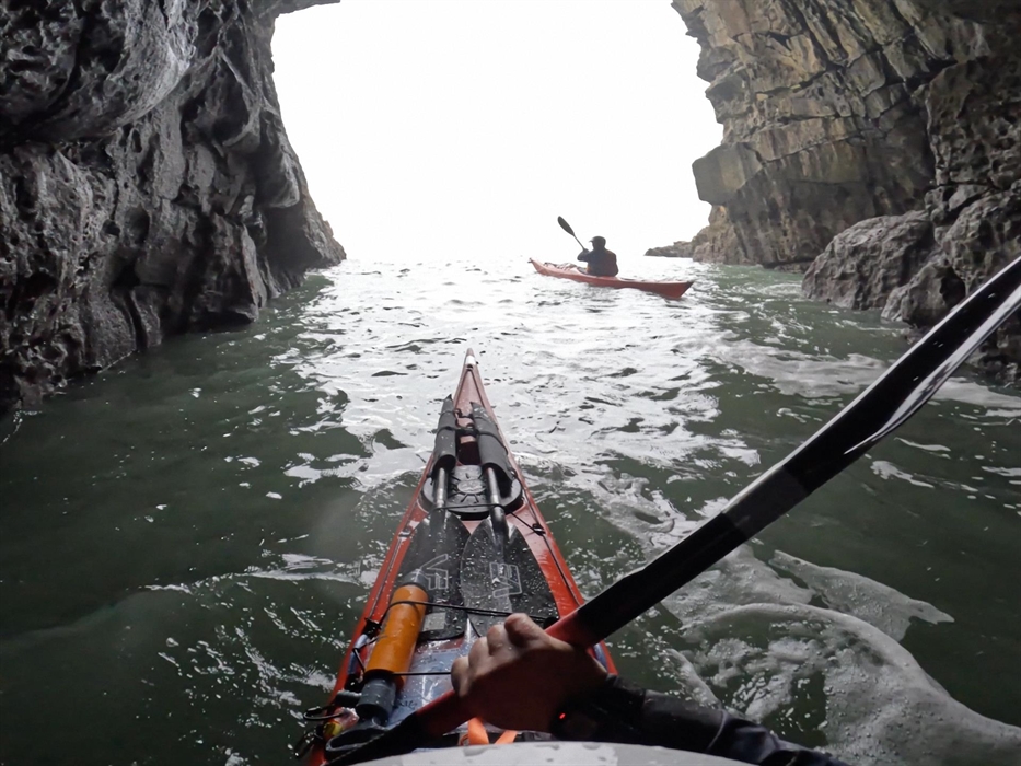 Two people in sea kayaks paddling out of a large cave