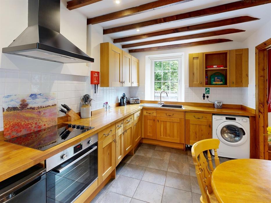 Warm wooden kitchen with beamed ceiling, electric hob, and countryside views through the window.