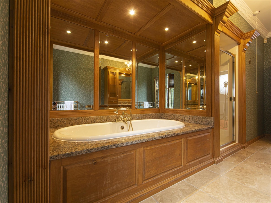 Elegant bathroom featuring a deep granite-surround bathtub, mirrored wood paneling, and vintage wallpaper for a classic country manor feel.