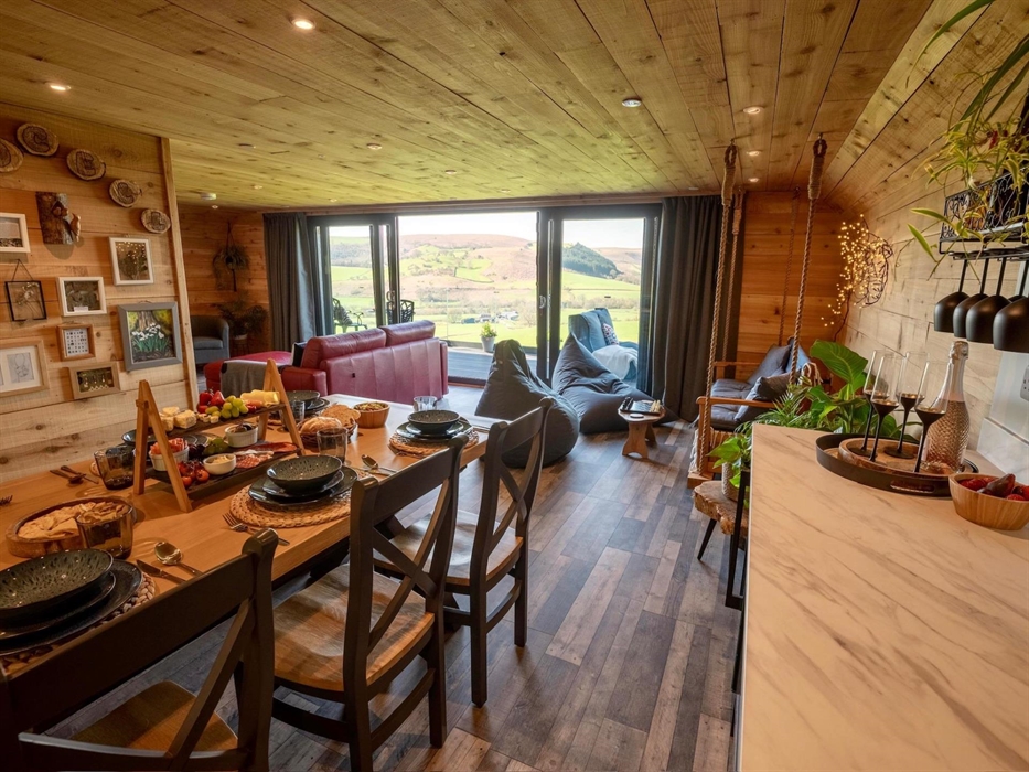 Open-plan living space features a lounge, swinging bench, fully equipped kitchen, and dining area with a wooden table for up to seven guests