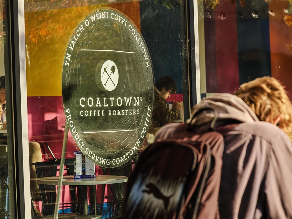 a window with the Coaltown Coffee logo and a man with a bag and coat walking past