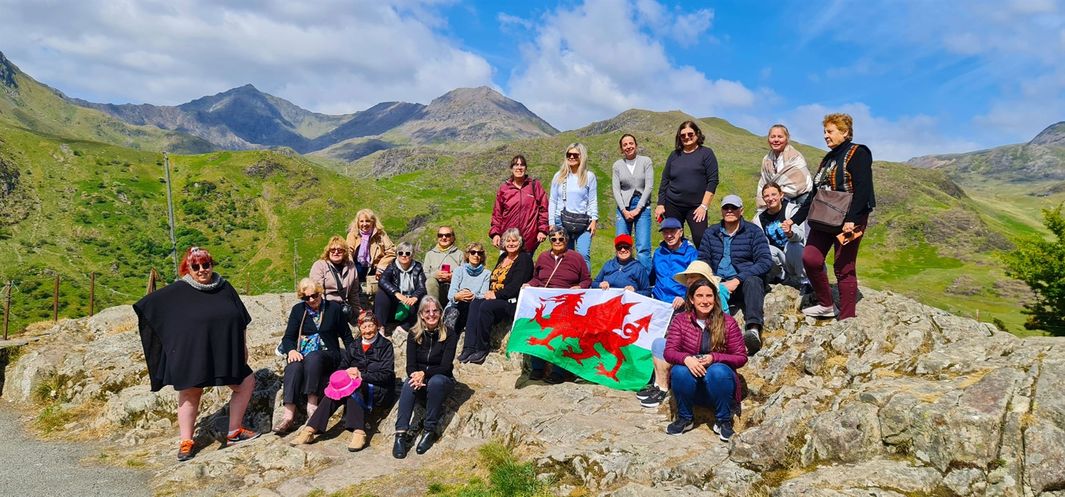 A group of people holding a Welsh flag on a mountain.