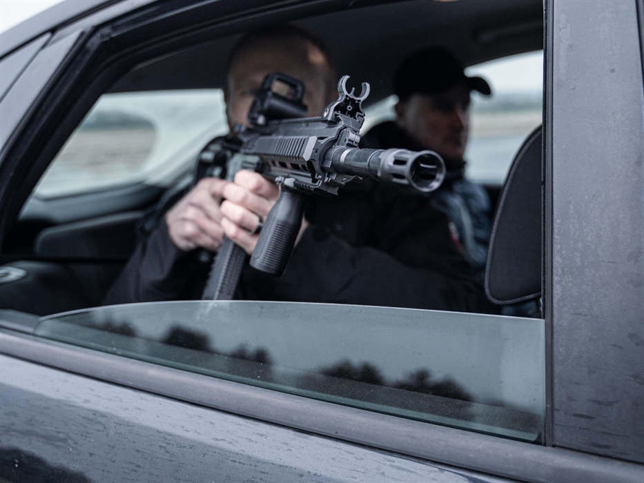 Man holding rifle from the rear of a vehicle