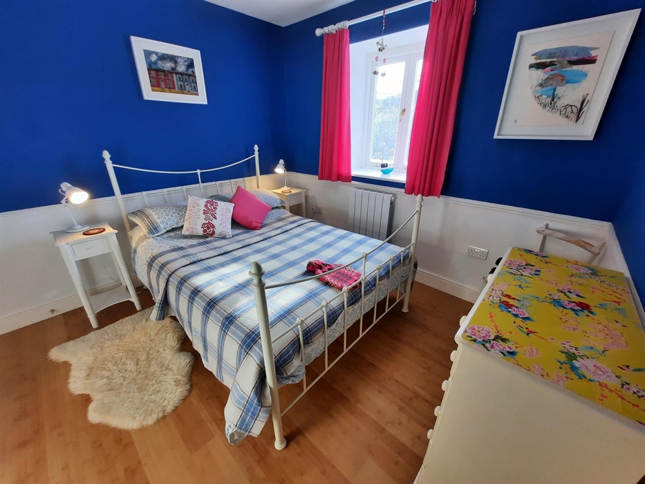 Cwt Mochyn double bedroom with blue walls, pink curtains and blue/pink Welsh blanket and hot water bottle
