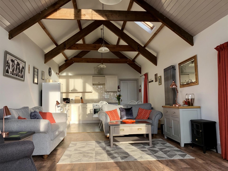 Bright and sunny kitchen diner with comfy sofas in the living area under original beamed vaulted ceiling