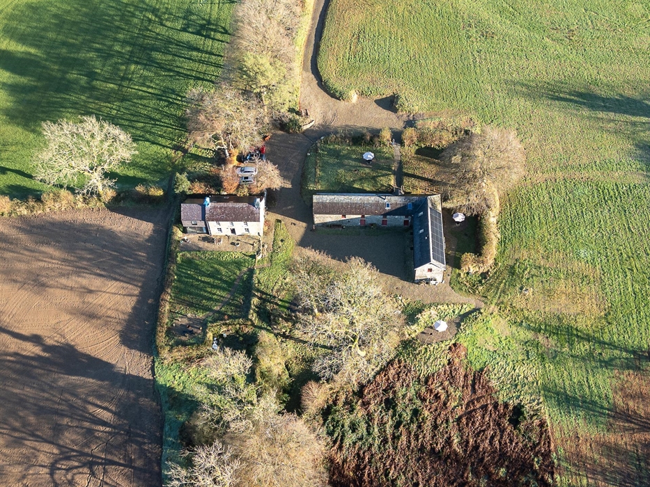 An aerial view of the house and barn during the winter, surrounded by fields and woodland