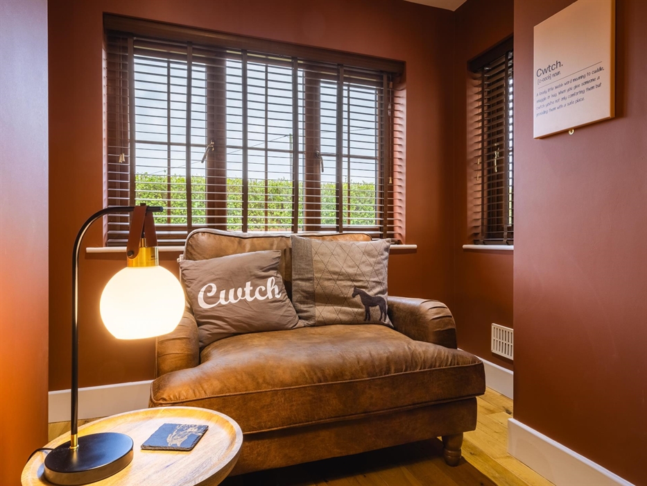 Large, two person Cwtch cuddle chair in a recess within the living room with Cwtch cushion and Cwtch sign and coffee table with reading lamp.