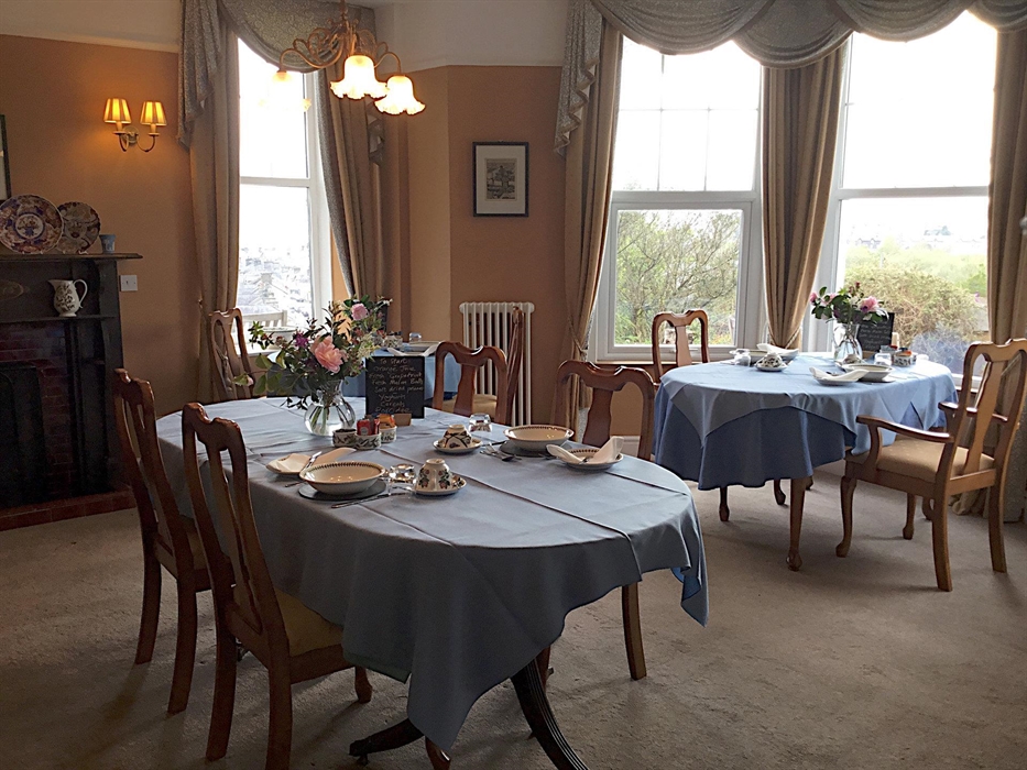 View of the dining room showing three tables set for breakfast, and large windows overlooking the garden and the village of Penrhyndeudraeth