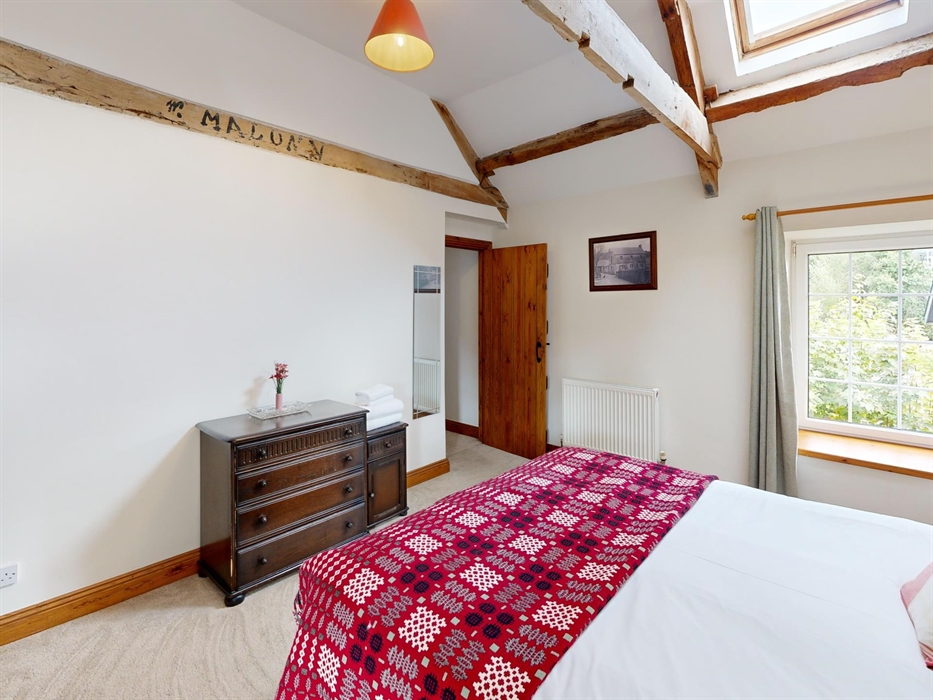A spacious king-size bedroom with exposed beams, heritage furniture, and a red traditional Welsh tapestry blanket adding warmth and character.