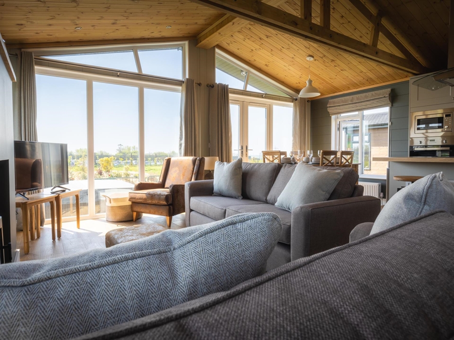 Sofas and faux, brown leather armchair facing flat screen smart TV, breakfast bar and dining table in background.
